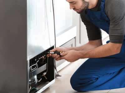 Male technician is repairing refrigerator indoors